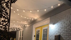 A covered outdoor area with a yellow door, a brick wall, and string lights.