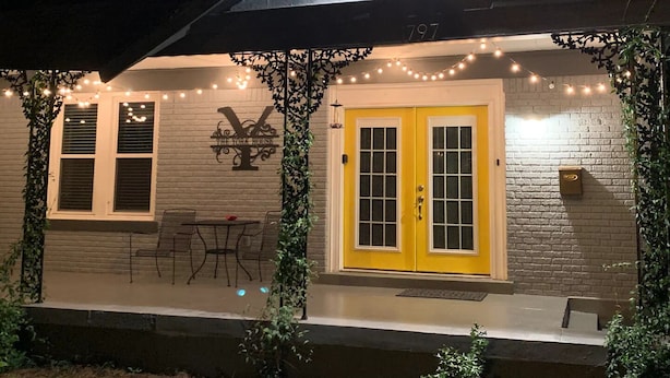 A house with a yellow door, a balcony with string lights, and a 'Y' sign on the wall.