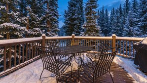 A wooden deck with metal chairs and a table, surrounded by snow-covered trees.