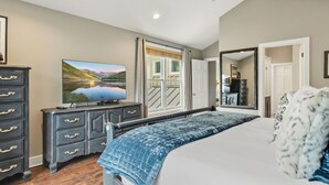 A bedroom with a large bed, a dresser, a television, and a view of a balcony.