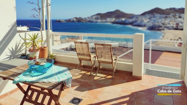A balcony with a table, chairs, and potted plants. It overlooks a beach and the sea. - EL CABO III        . (San José)