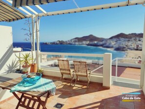 A balcony with a table, chairs, and potted plants. It overlooks a beach and the sea. - EL CABO III        . (San José)