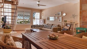 A spacious living room with a wooden table, comfortable seating, a ceiling fan, and a view through large windows. - EL CABO III        . (San José)