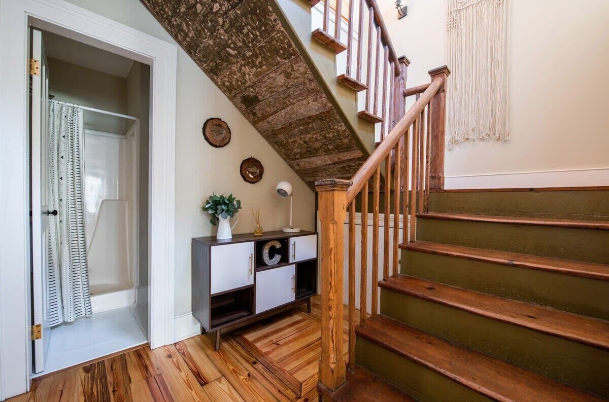 Un escalier avec des marches en bois et une rampe en bois, menant à un palier où se trouve une console blanche et une plante.