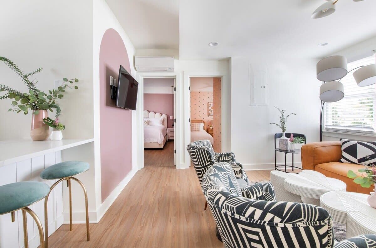 Ein modernes Wohnzimmer mit Sofa, Sesseln und Couchtisch. Ein Fernseher ist an der Wand montiert und auf dem Beistelltisch steht eine Pflanze.