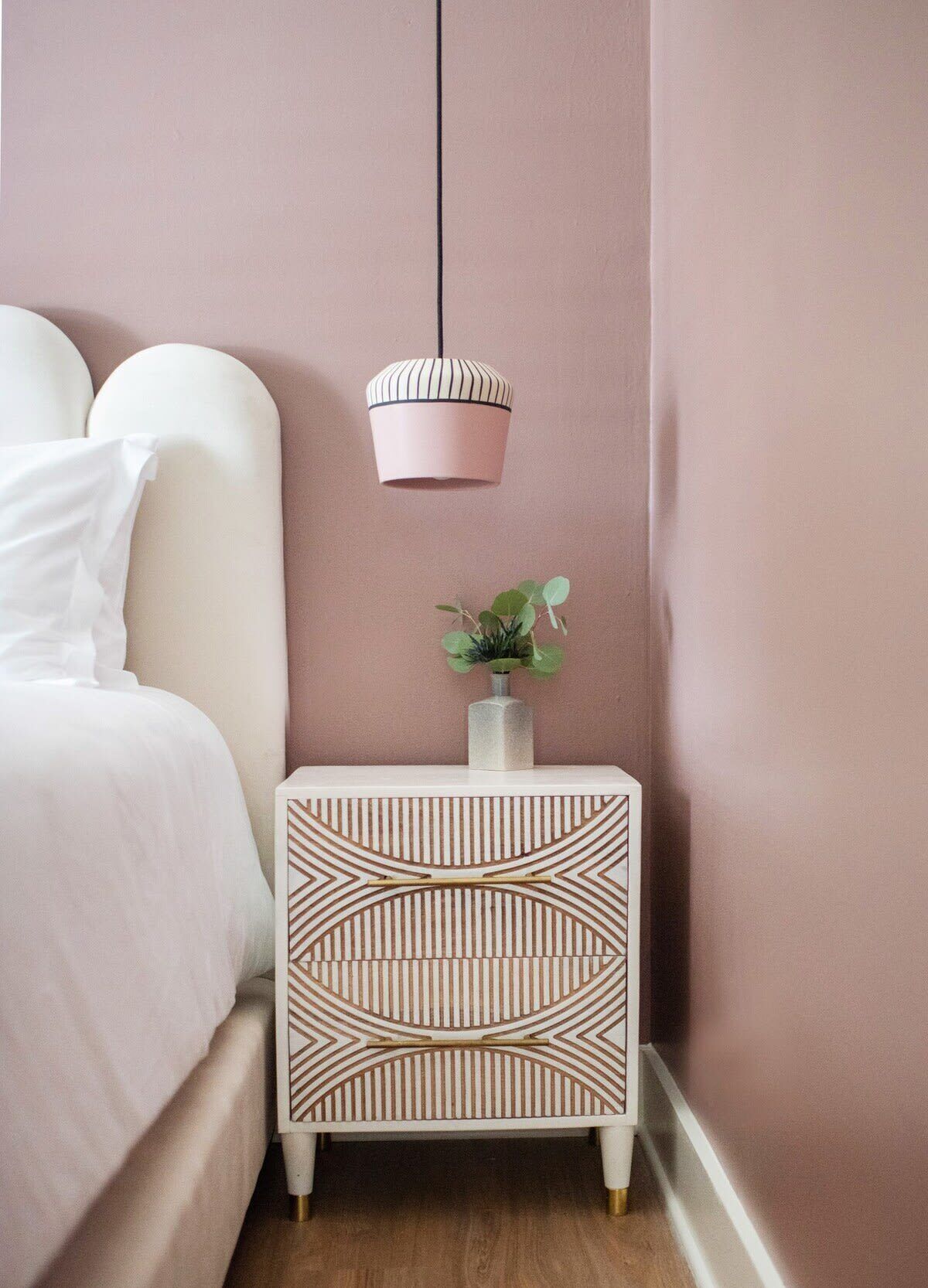 A neatly arranged bedroom with a bed, a bedside table with a decorative lamp, and a potted plant.