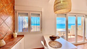 A kitchen with a view of the sea, a dining area with a table and chairs, and a hanging light fixture.
