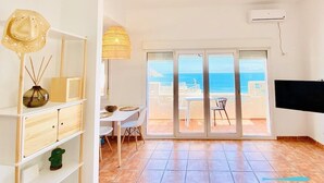 A spacious room with a large sliding glass door leading to a balcony with a view of the sea.