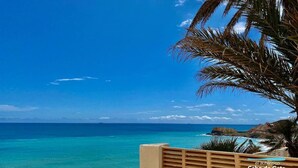 A coastal view with a clear sky, turquoise sea, and a wooden balcony overlooking the ocean.