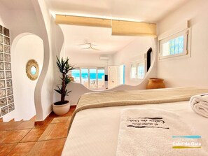 A spacious bedroom with a large bed, a potted plant, and a view of the ocean through a large window. - Casa Gloria        . (Ventorros de San José)