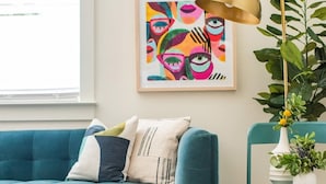 Un canapé de couleur turquoise agrémenté de coussins, un fauteuil en osier, une lampe sur pied, une petite table avec un vase et deux œuvres d’art encadrées accrochées au mur.