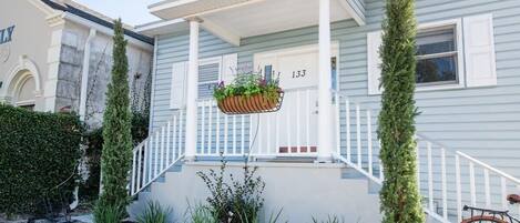 Una casa con porche, un macramé con flores, una bicicleta y el número 133 en la puerta.