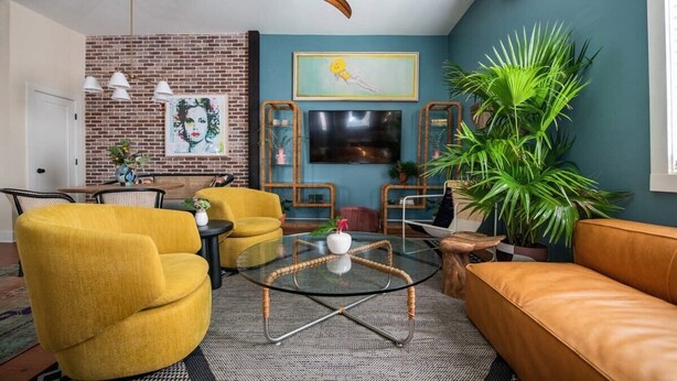 A living room with a brick wall, a large plant, and a yellow sofa. - Soho House | Prime Location, Walk to Everything! (Charleston)