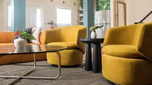 A living room with yellow armchairs, a glass coffee table, and a small side table with a vase. - Soho House | Prime Location, Walk to Everything! (Charleston)