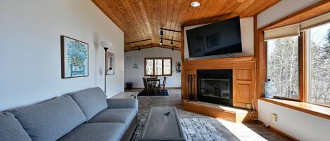 Una sala de estar moderna con un sofá seccional gris, una mesa de centro, una chimenea y un televisor montado en la pared.