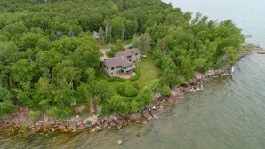 Une vue aérienne d’une maison entourée d’une forêt dense, avec une côte rocheuse au premier plan.