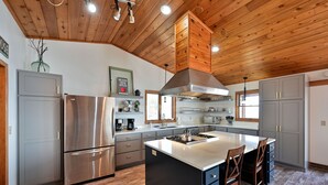 Une cuisine moderne dotée d’un grand îlot central, d’appareils électroménagers en acier inoxydable et d’un plafond en bois.