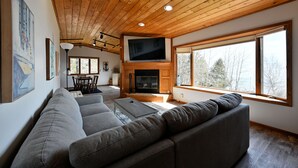 Un salon moderne avec un plafond en bois, une cheminée, un grand téléviseur et un canapé.