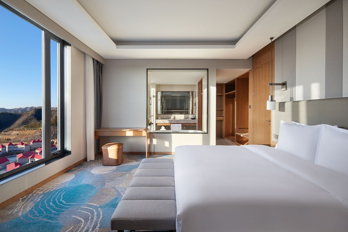 A modern hotel room with a large bed, a desk, and a bathroom.
