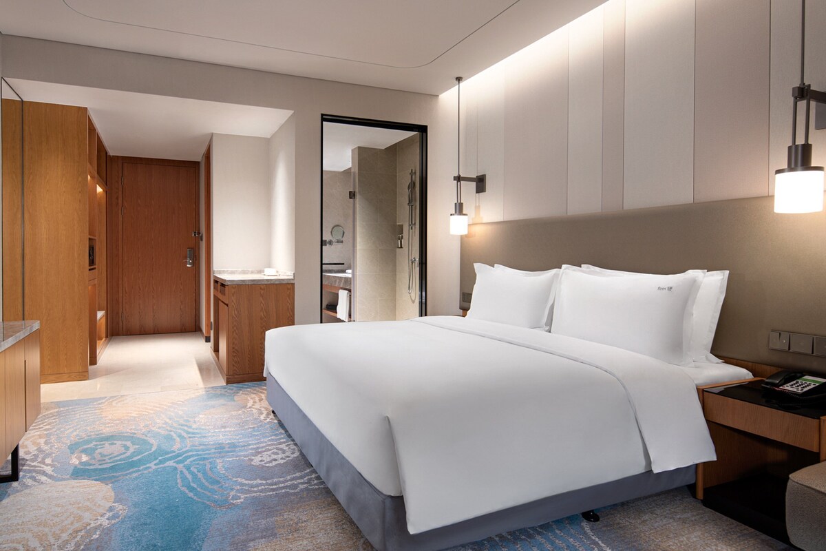 A hotel room with a bed, a desk, a TV, and a bathroom visible through an open door.
