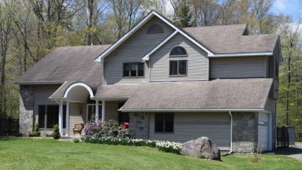 A two-story house with a stone foundation, a covered porch, and a well-maintained lawn. - Spacious House near Lake and Snowmobile Trails (Piseco)
