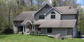 Stunning two-story home with a central entrance and covered porch, set amidst a beautifully manicured lawn and lush trees.