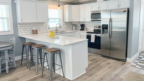 A modern kitchen with white cabinets, a stainless steel refrigerator, and a central island with stools. - Beachfront Cabin with Lake Views & Harry Potter Room (Annandale)