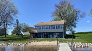 A two-story house with a deck and a dock extending into a calm body of water. - Beachfront Cabin with Lake Views & Harry Potter Room (Annandale)