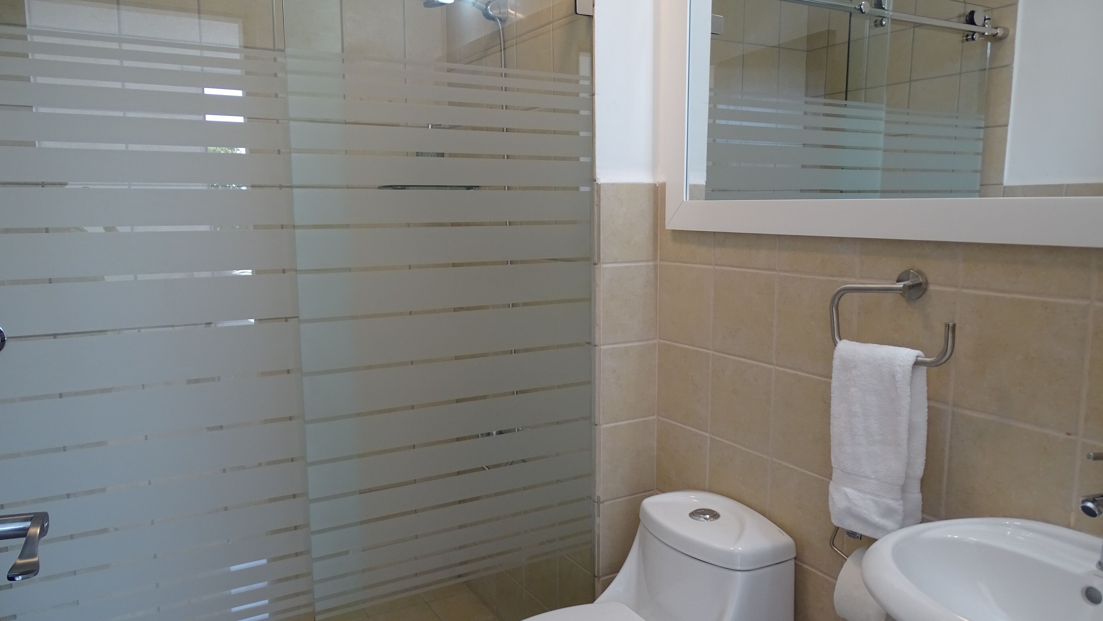 Un baño con cabina de ducha de vidrio, inodoro, lavabo y perchero para toallas.