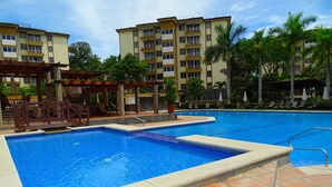 A swimming pool with a tiled deck, surrounded by palm trees and a multi-story building with balconies. - Penthouse Jaco Beach - 3Room (Jacó)