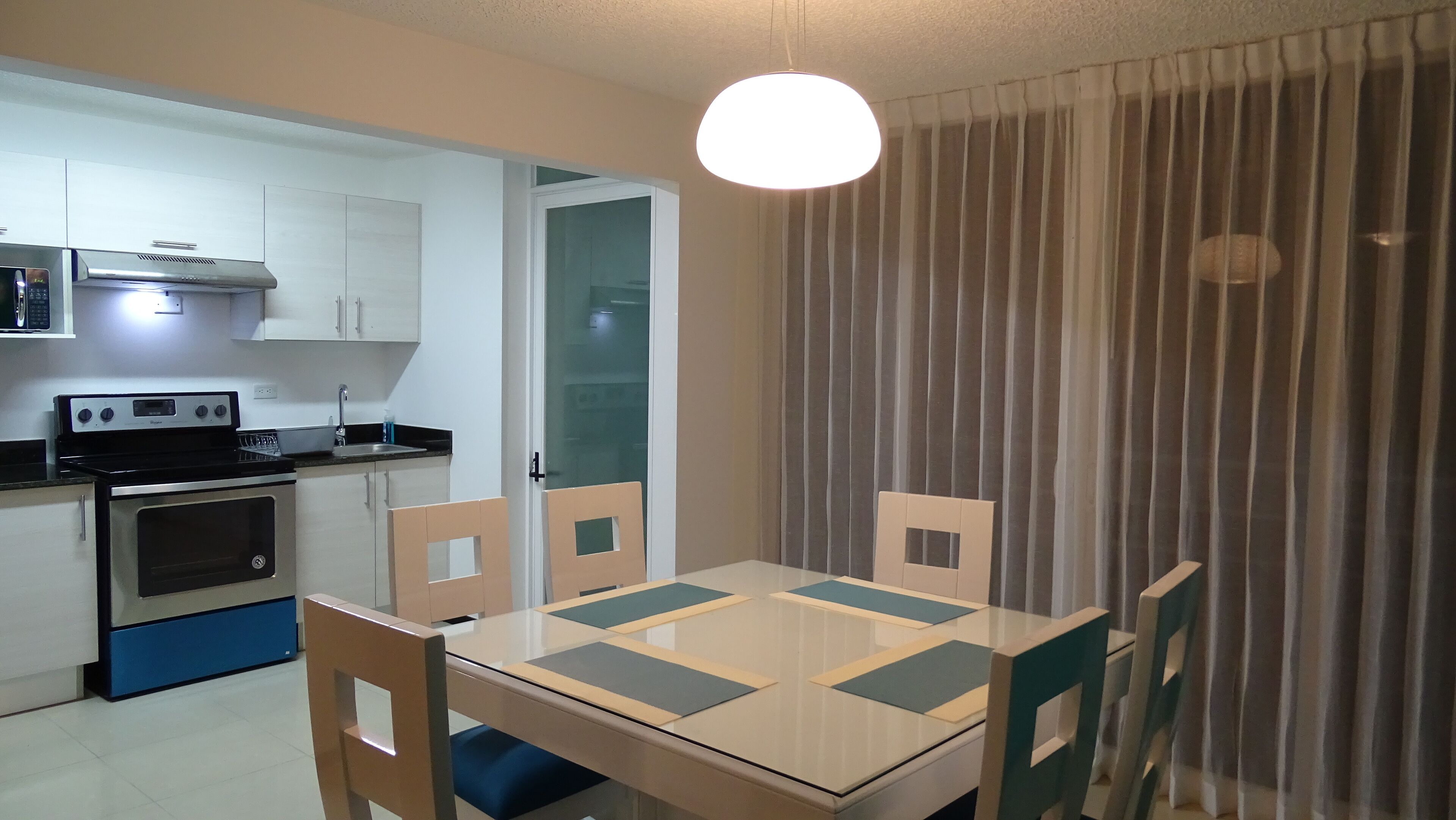 Una cocina compacta con estufa, horno y microondas, una mesa de comedor con sillas y una ventana con cortina.