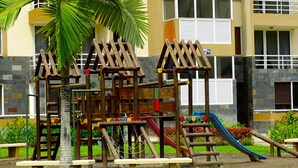 A playground with climbing structures and slides, surrounded by a building with balconies and windows. - Penthouse Jaco Beach - 3Room (Jacó)