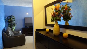 A modern living room with a black sofa, a television, a vase with flowers, and a large mirror on the wall. - Penthouse Jaco Beach - 3Room (Jacó)