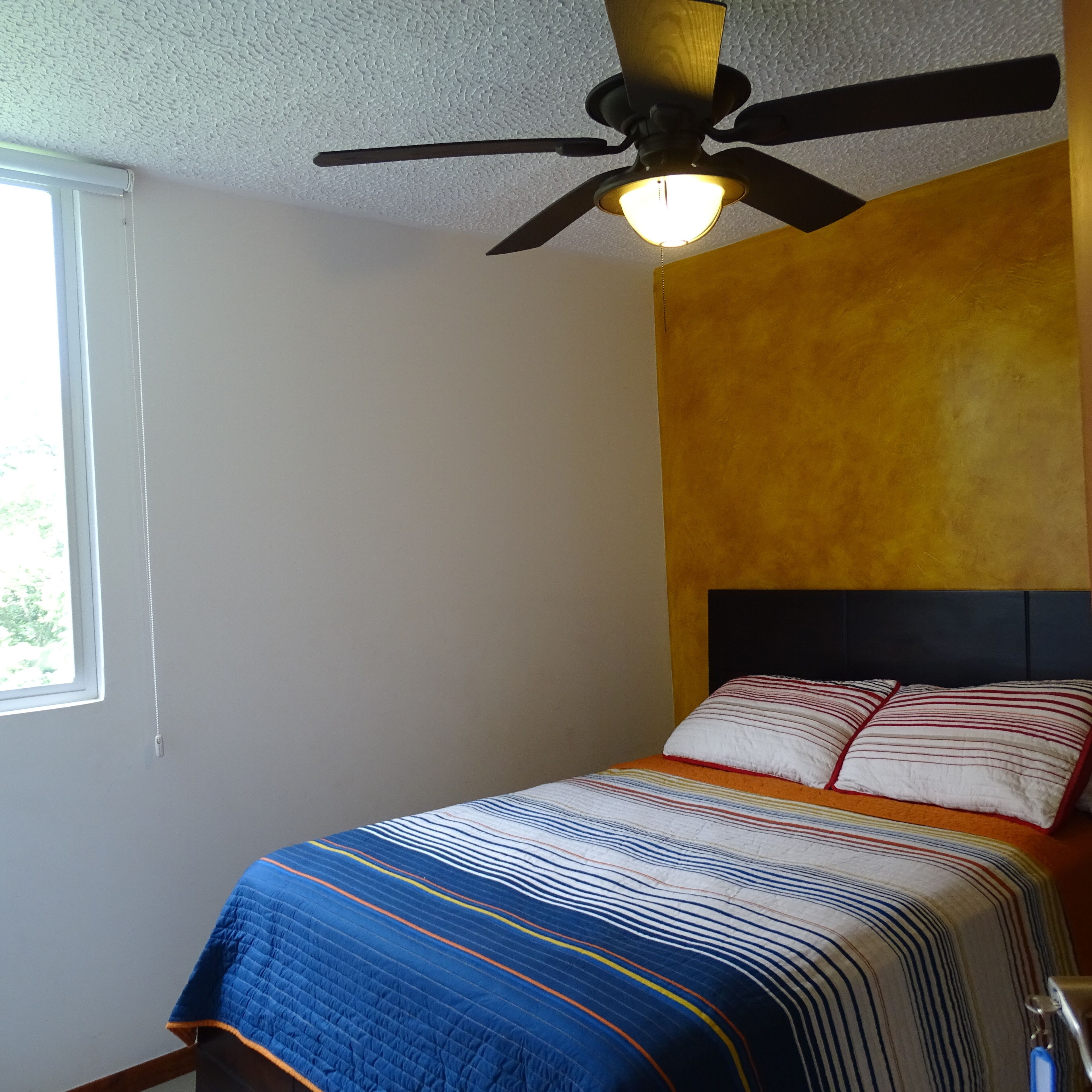 Un dormitorio con cama, ventilador de techo y ventana.