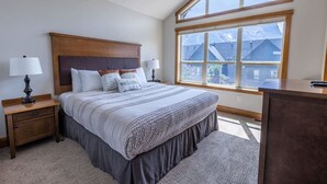 A bedroom with a large bed, two bedside tables, a desk, and a window with a view of buildings.