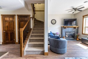A staircase leading to a second floor, a living room with a fireplace, a television, and a ceiling fan.