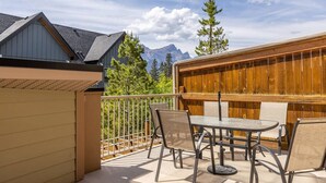 A balcony with a table and chairs, a wooden fence, and a mountain view.