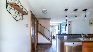 A modern kitchen with a built-in dishwasher, a wooden staircase, and pendant lights.
