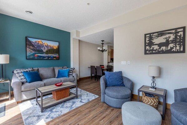 Una sala de estar moderna con un sofá, sillones, una mesa de centro y un cuadro de un paisaje montañoso.