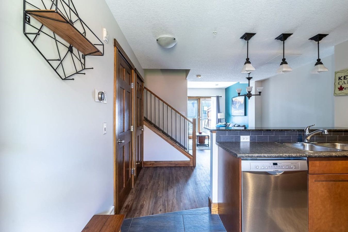 A modern kitchen with a built-in dishwasher, a wooden staircase, and pendant lights.