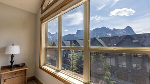 A room with large windows offering a mountain view, a wooden nightstand with a lamp, and a carpeted floor.