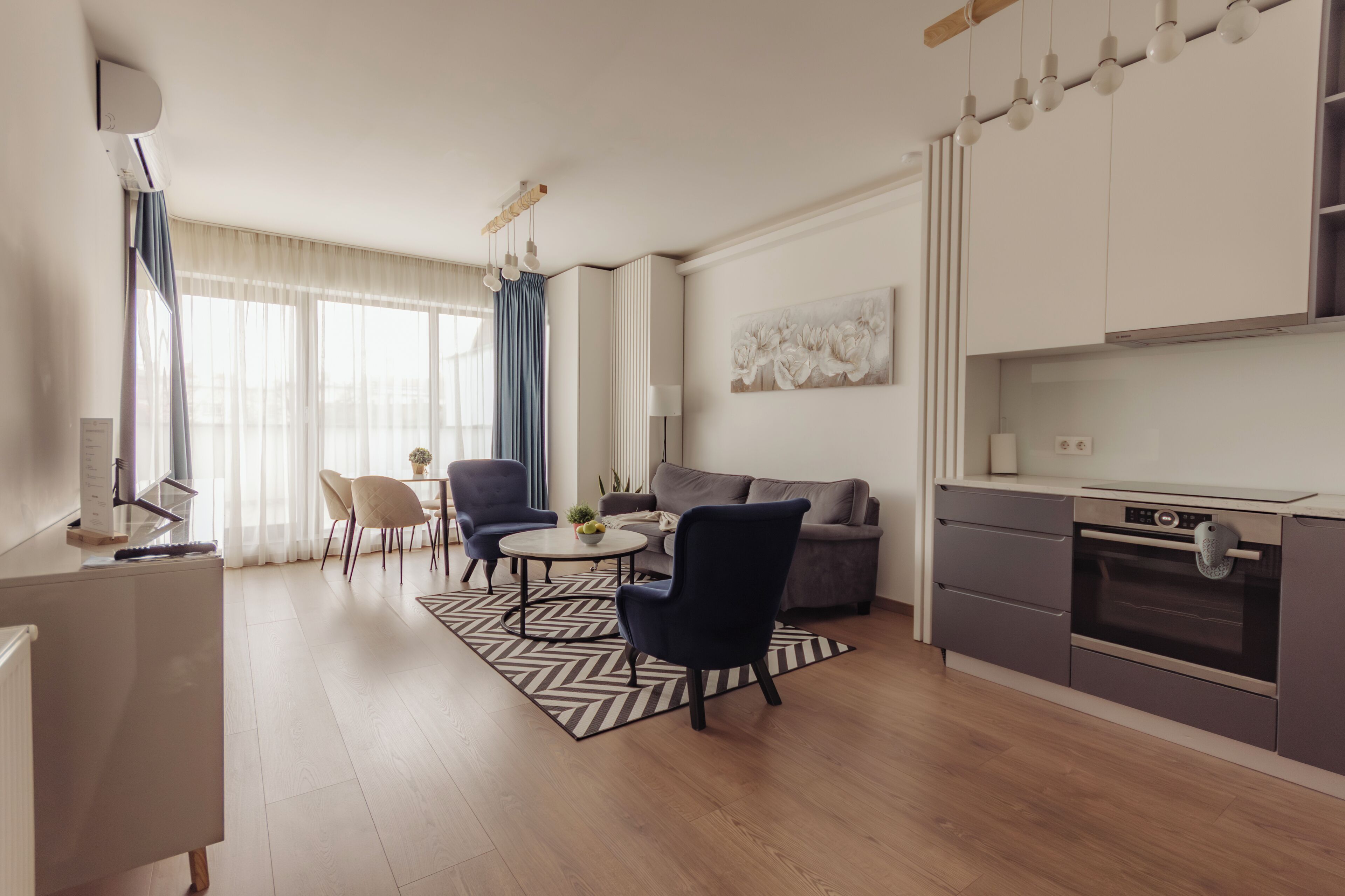 A modern kitchen with a built-in oven, a dining area with a round table and chairs, and a living area with a sofa and a coffee table.