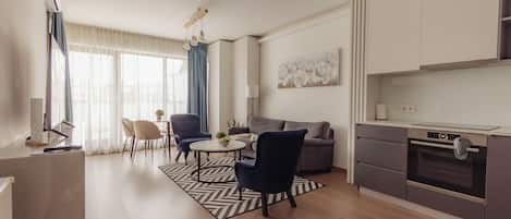 A modern kitchen with a built-in oven, a dining area with a round table and chairs, and a living area with a sofa and a coffee table.