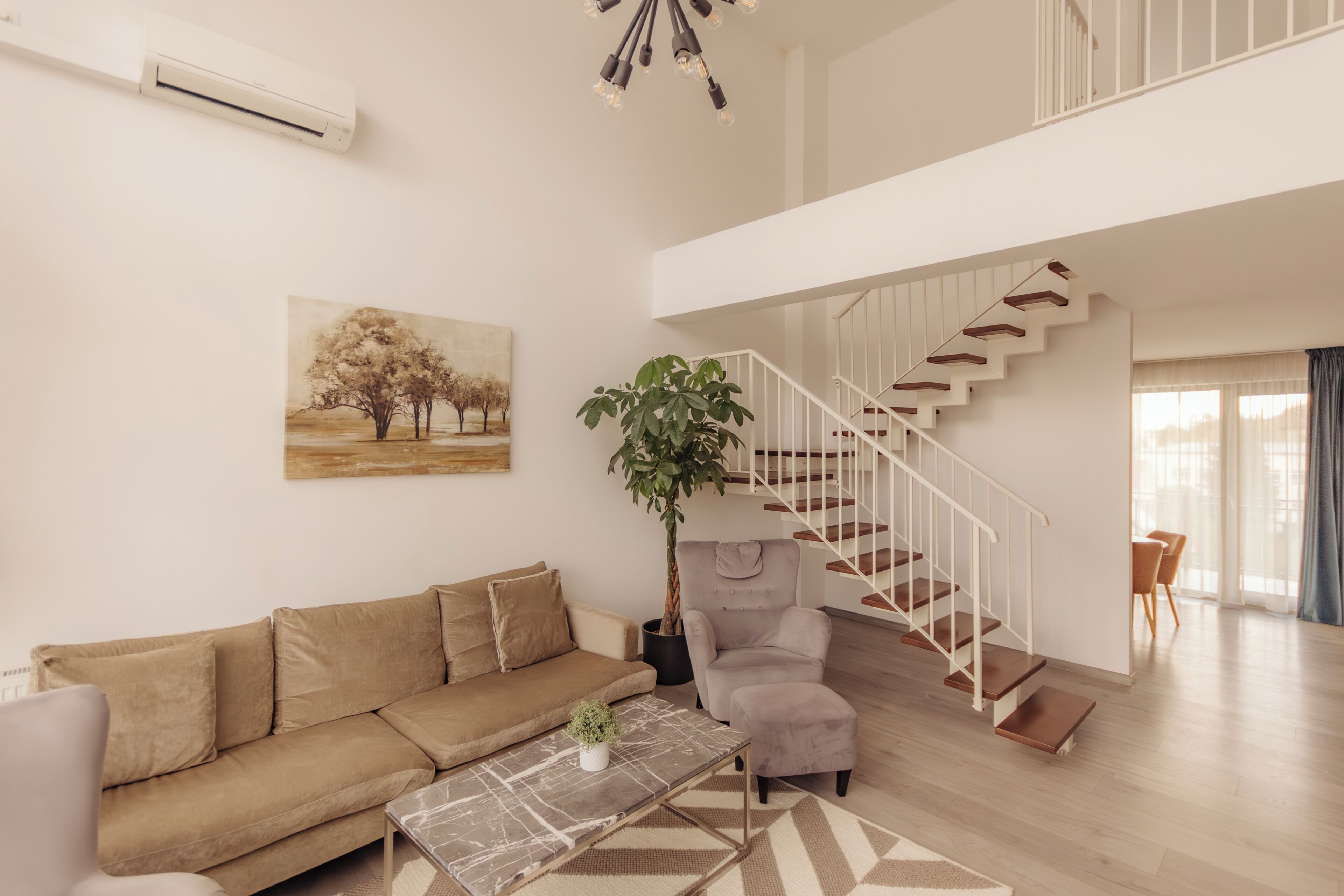 A living room with a sofa, armchair, coffee table, and a staircase.