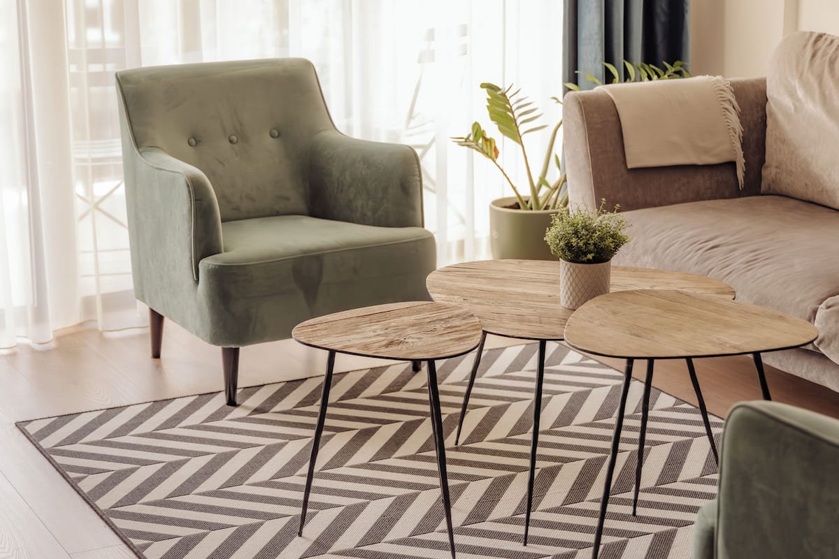Una sala de estar con un sillón verde, un sofá color beige y dos mesas redondas de madera.