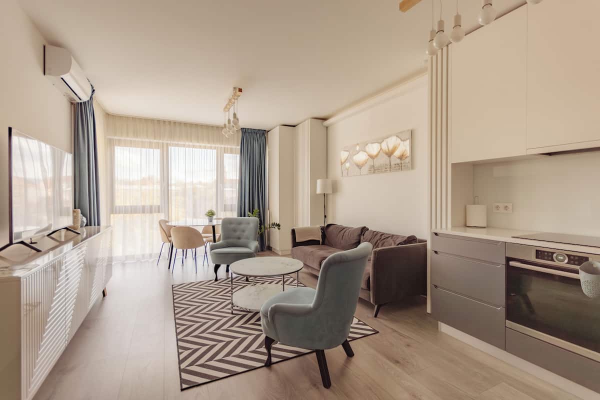 Una sala de estar moderna con un sofá, sillones, una mesa de centro y una zona de cocina con horno.