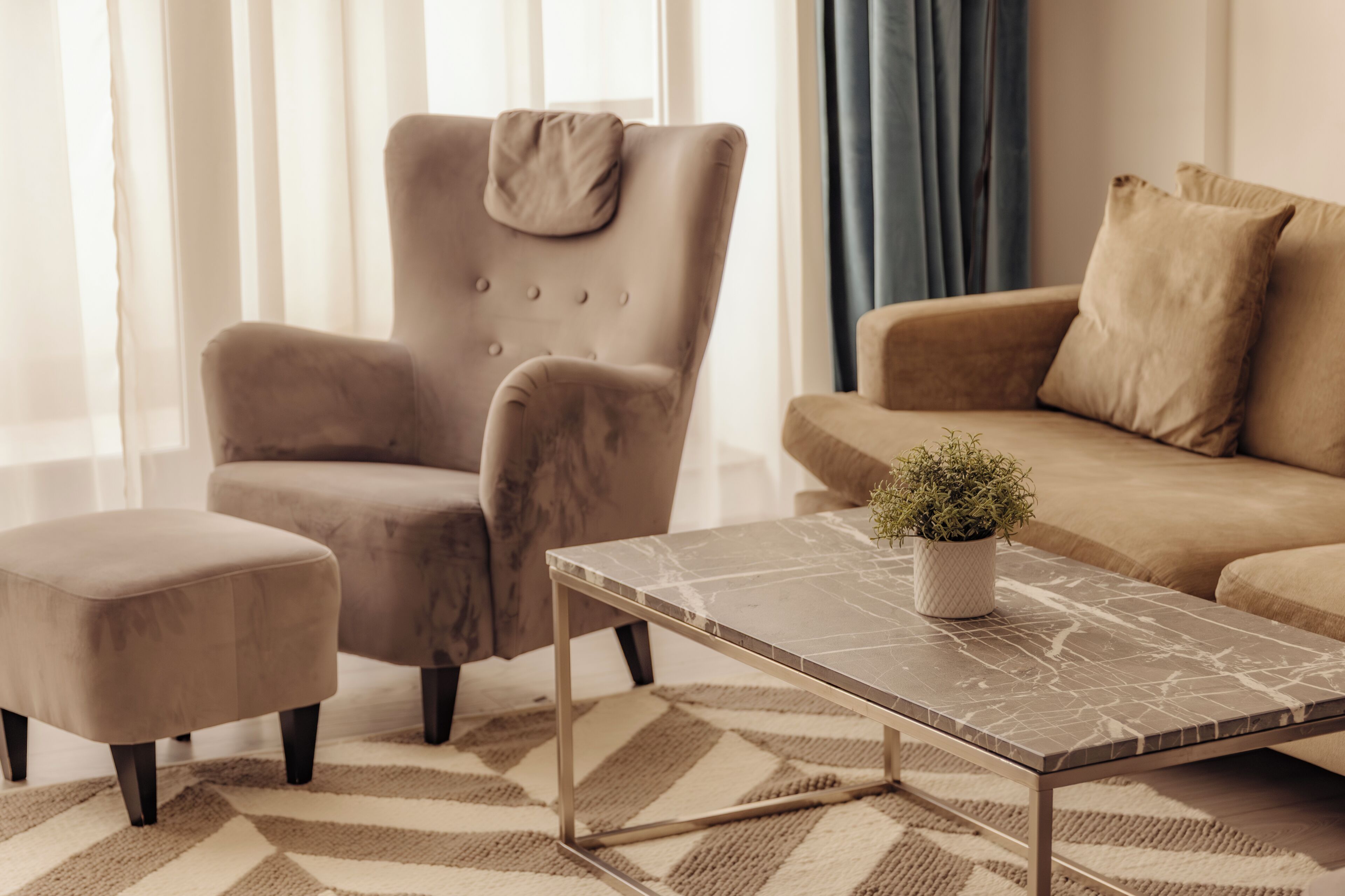 Un salon comprenant un canapé, un fauteuil, un pouf et une table basse agrémentée d’une plante.