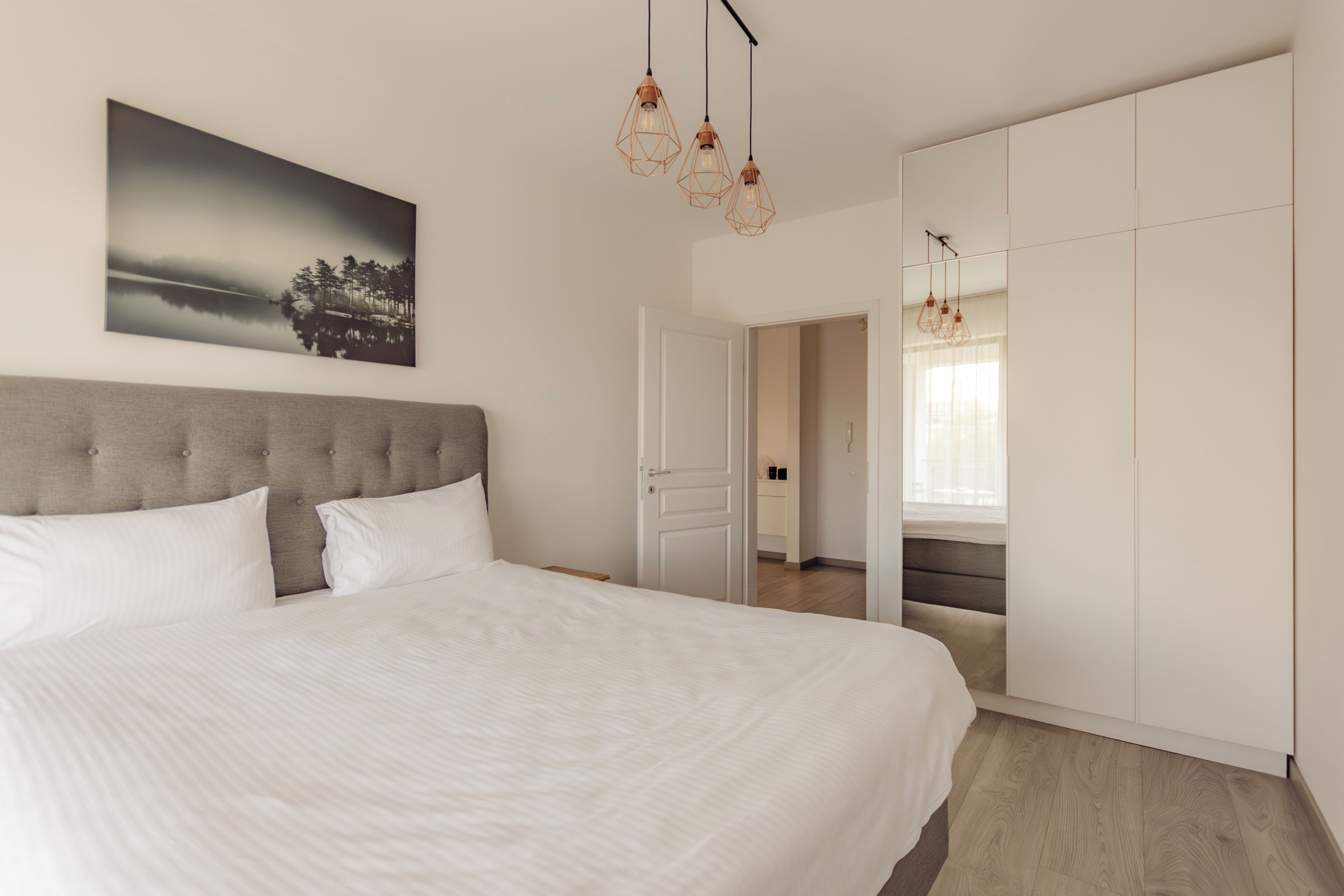 A bedroom with a large bed, a headboard, a wardrobe, and a painting on the wall.