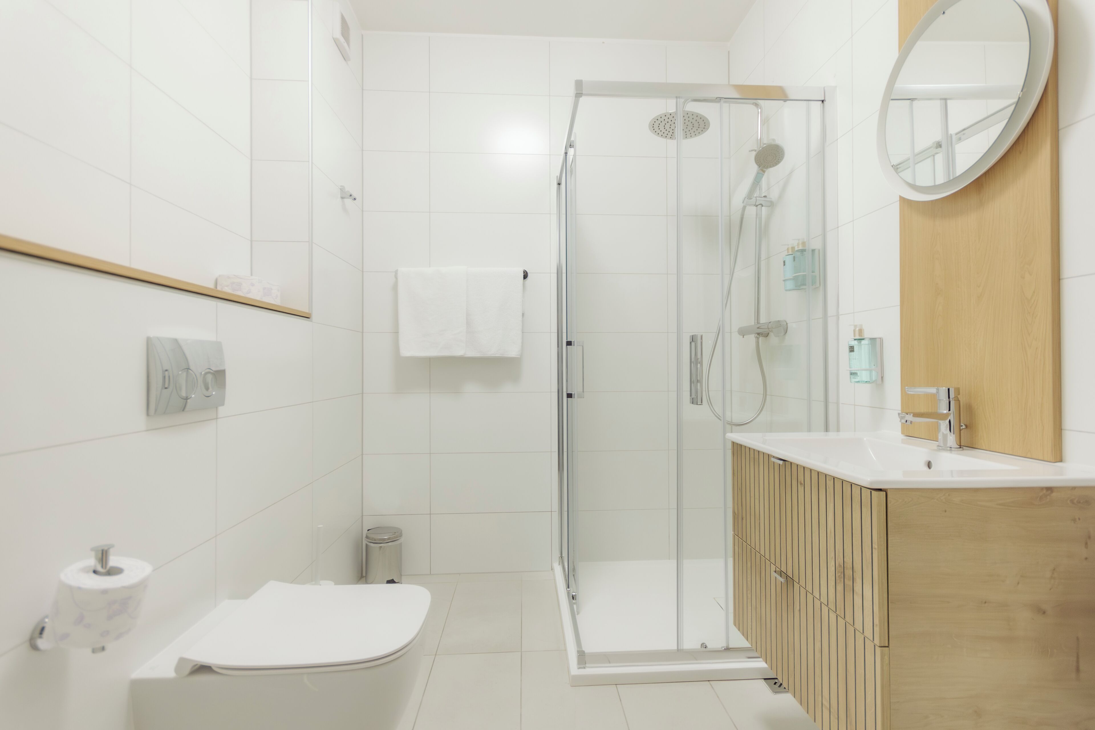 Une salle de bain moderne avec une douche à parois de verre, un meuble-lavabo en bois et des toilettes blanches.