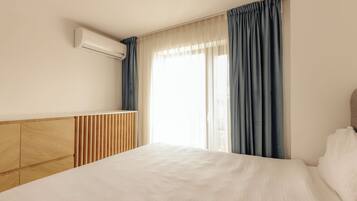 A hotel room with a bed, a wooden headboard, a built-in air conditioning unit, and a window with curtains.